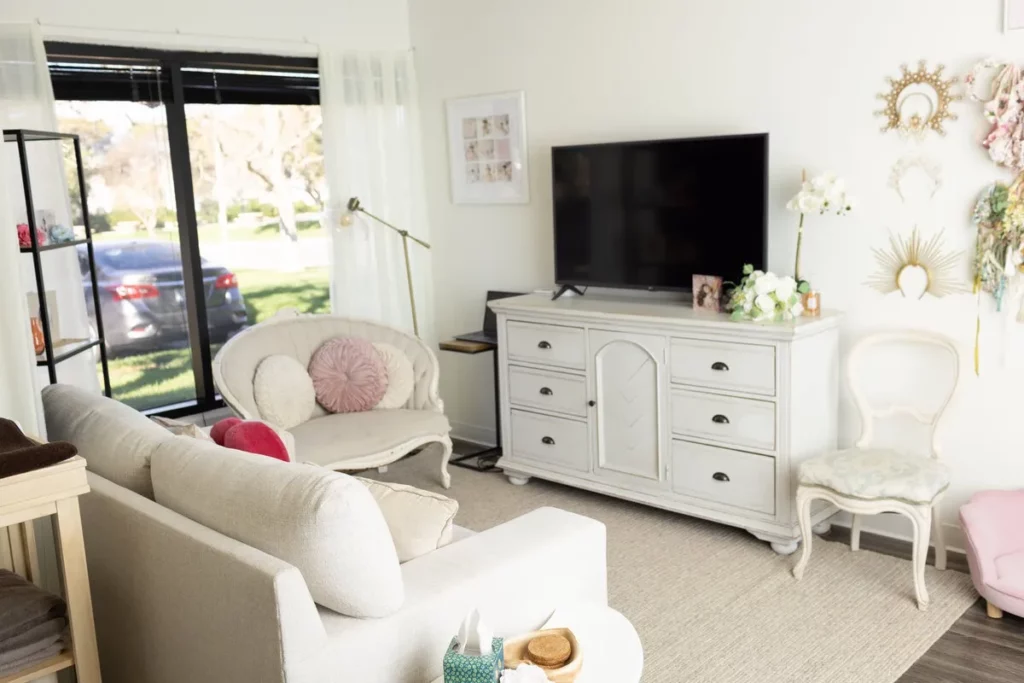 Bright living room with a sofa, TV on a white dresser, decorative pillows, a chair, wall art, large windows, and natural light coming in. Lovely Baby Photography by Stacey Marsh