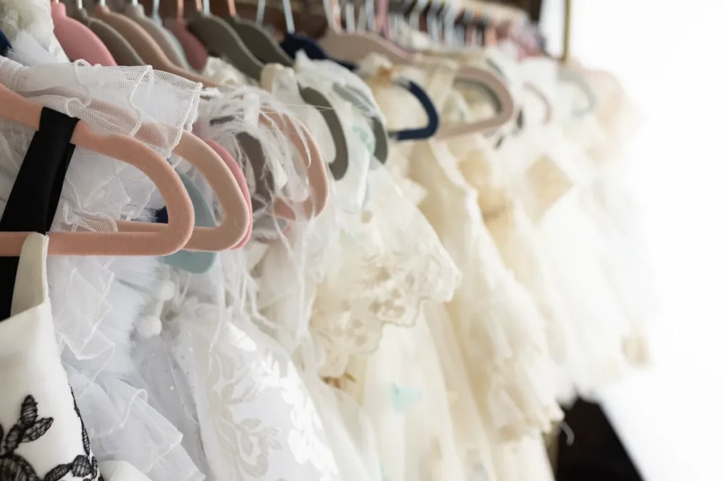 A row of white and cream lace dresses on hangers, displayed on a clothing rack. Lovely Baby Photography by Stacey Marsh