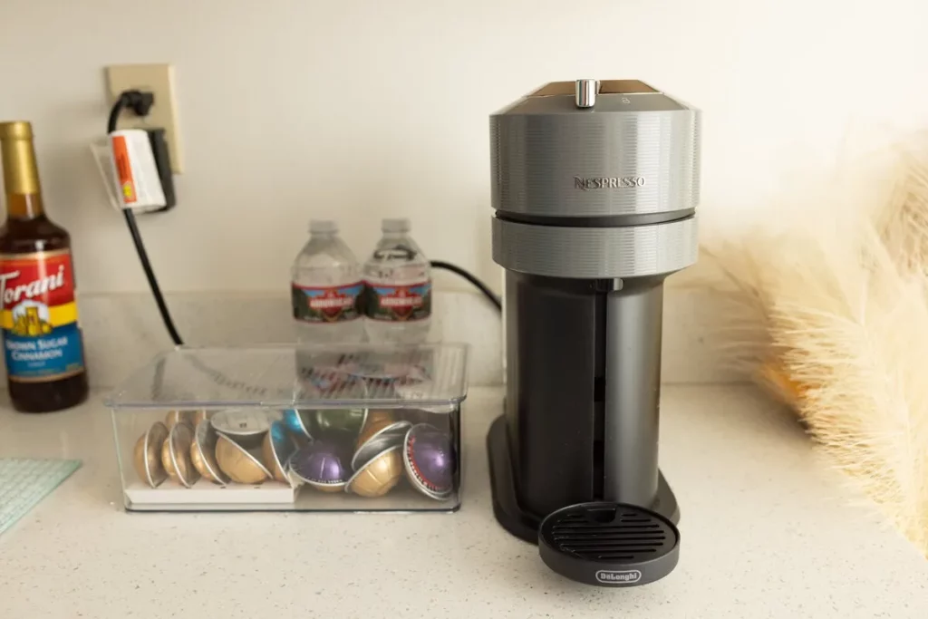 A Nespresso coffee machine sits on a kitchen counter next to a container of coffee pods, bottled water, and coffee syrup. Lovely Baby Photography by Stacey Marsh