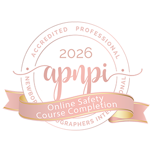 A circular badge displaying "2026 apmpi Accredited Professional Newborn Photographers International" with a ribbon stating "Online Safety Course Completion. Lovely Baby Photography, 2185 Faraday Ave suite 110, Carlsbad, CA 92008, +1 760-271-0725