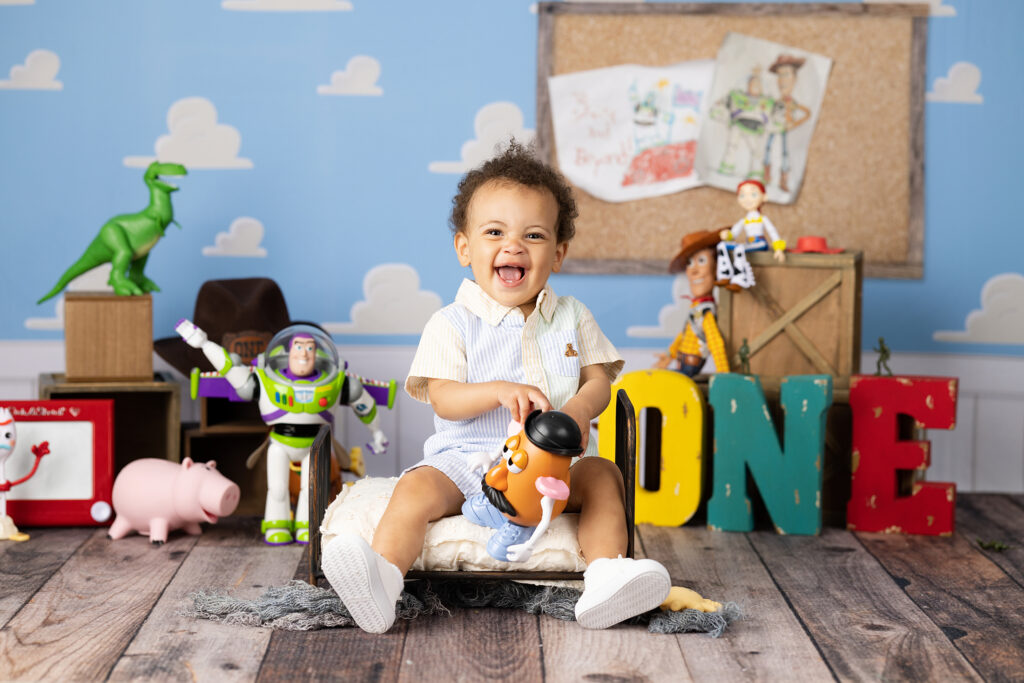 Carlsbad cake smash photographer offering Toy Story one year sessions with characters and colorful "ONE" letters, against a blue sky-themed backdrop—perfectly captured by a first birthday photographer Carlsbad. Lovely Baby Photography, 2185 Faraday Ave suite 110, Carlsbad, CA 92008, +1 760-271-0725
